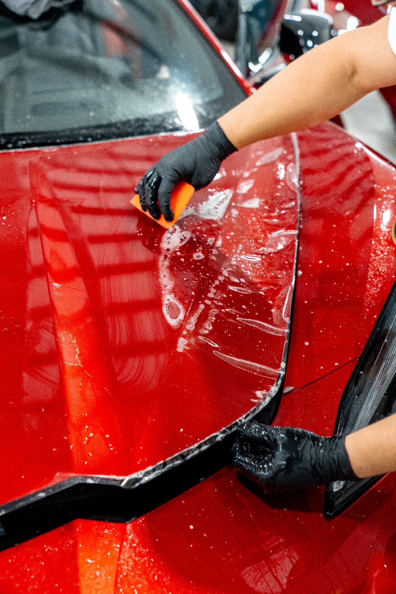 Installer laying paint protection film on a red sports car hood in the Fort Myers shop
